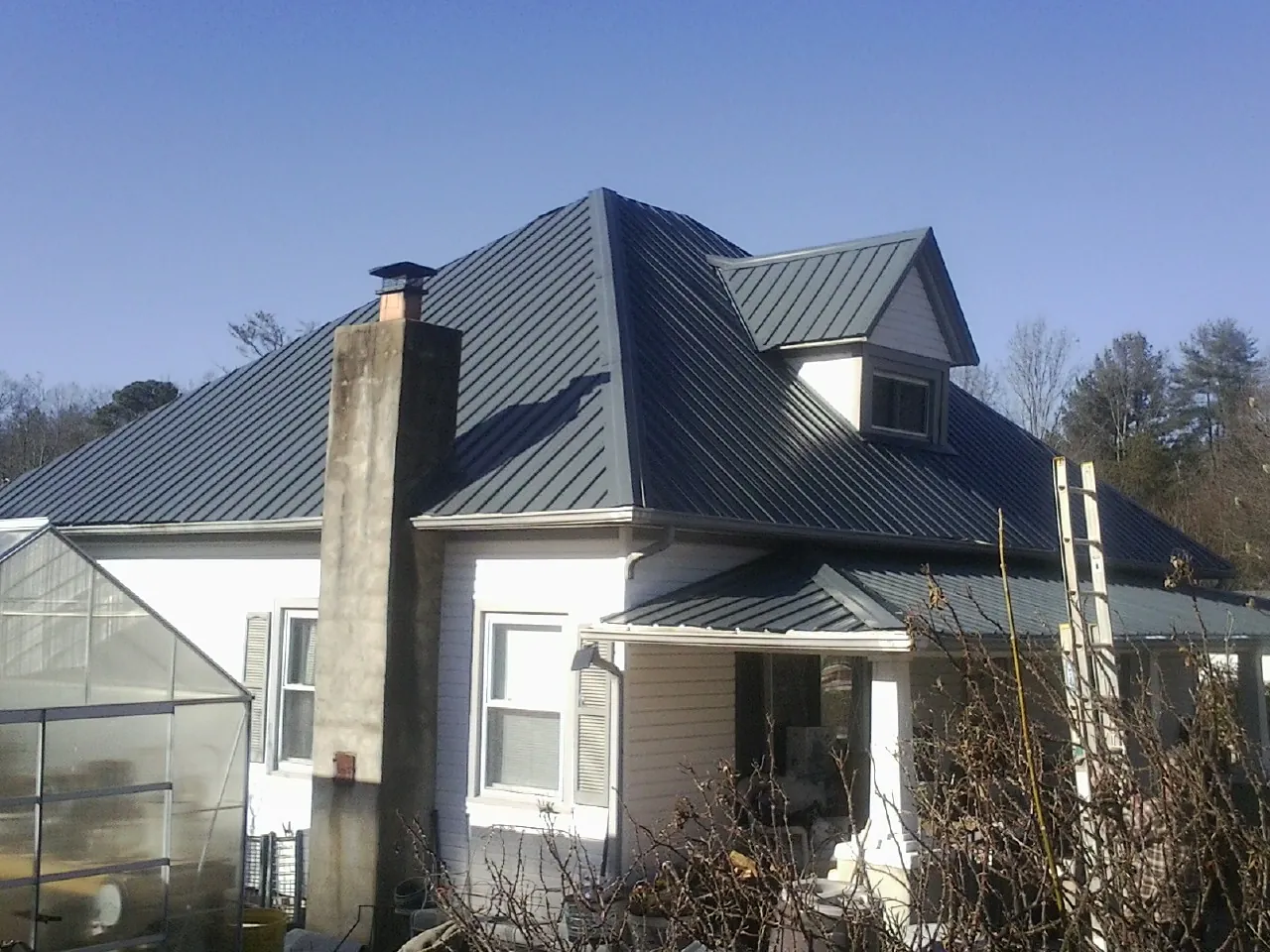 Dark blue standing seam metal roof on a white farmhouse with dormer — Slate & Tile Roof Repair by Roofing Brothers in Henniker