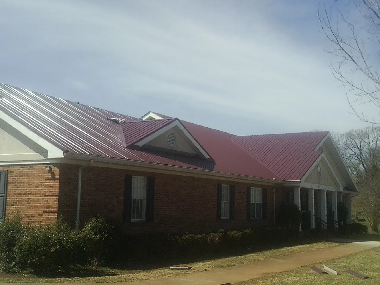 Red metal roof with gabled entries on a long brick building, from a Hail Damage Roof Repair job in Henniker