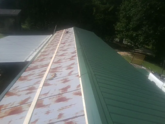 Old rusted panels beside newly installed green metal roofing — Wind Damage Roof Repair by Roofing Brothers in Henniker