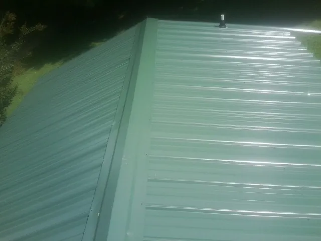 New green metal panels meeting at the ridge of a roof — Flat Roof Repair work by our crew in Henniker