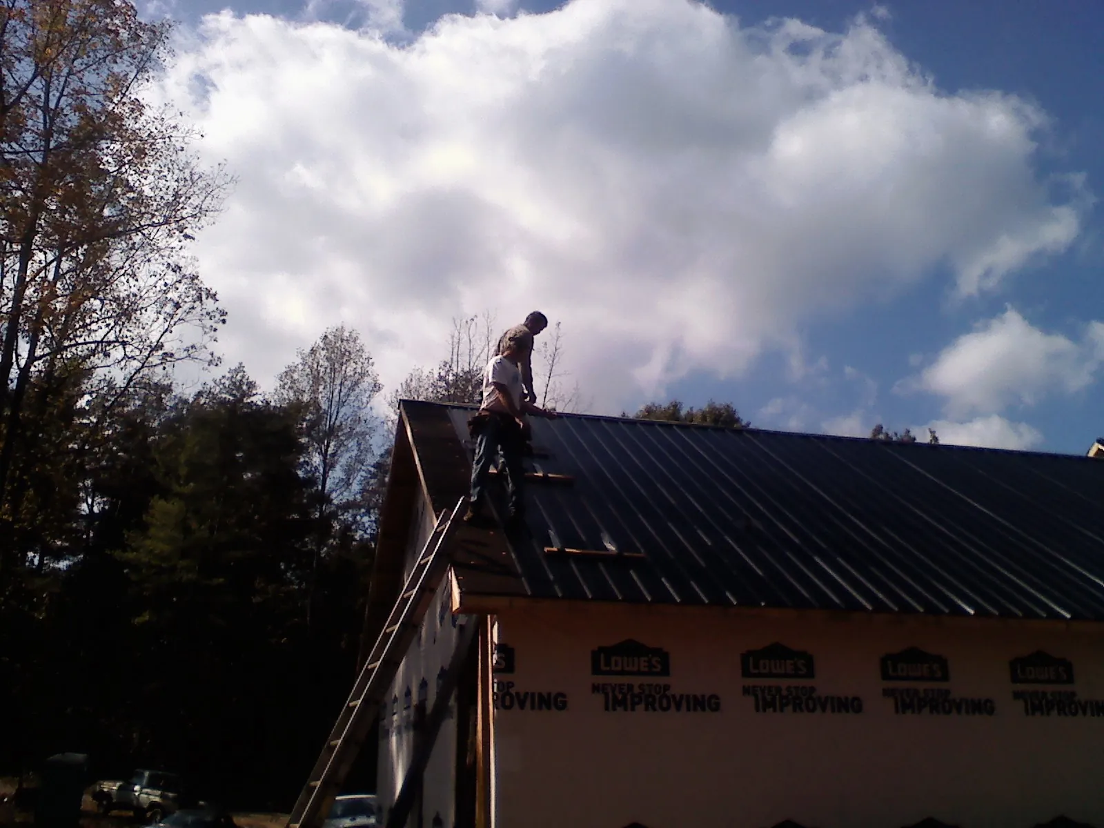 Roofer fastening dark metal panels high against a cloudy sky, from a Roof Inspection job in Henniker