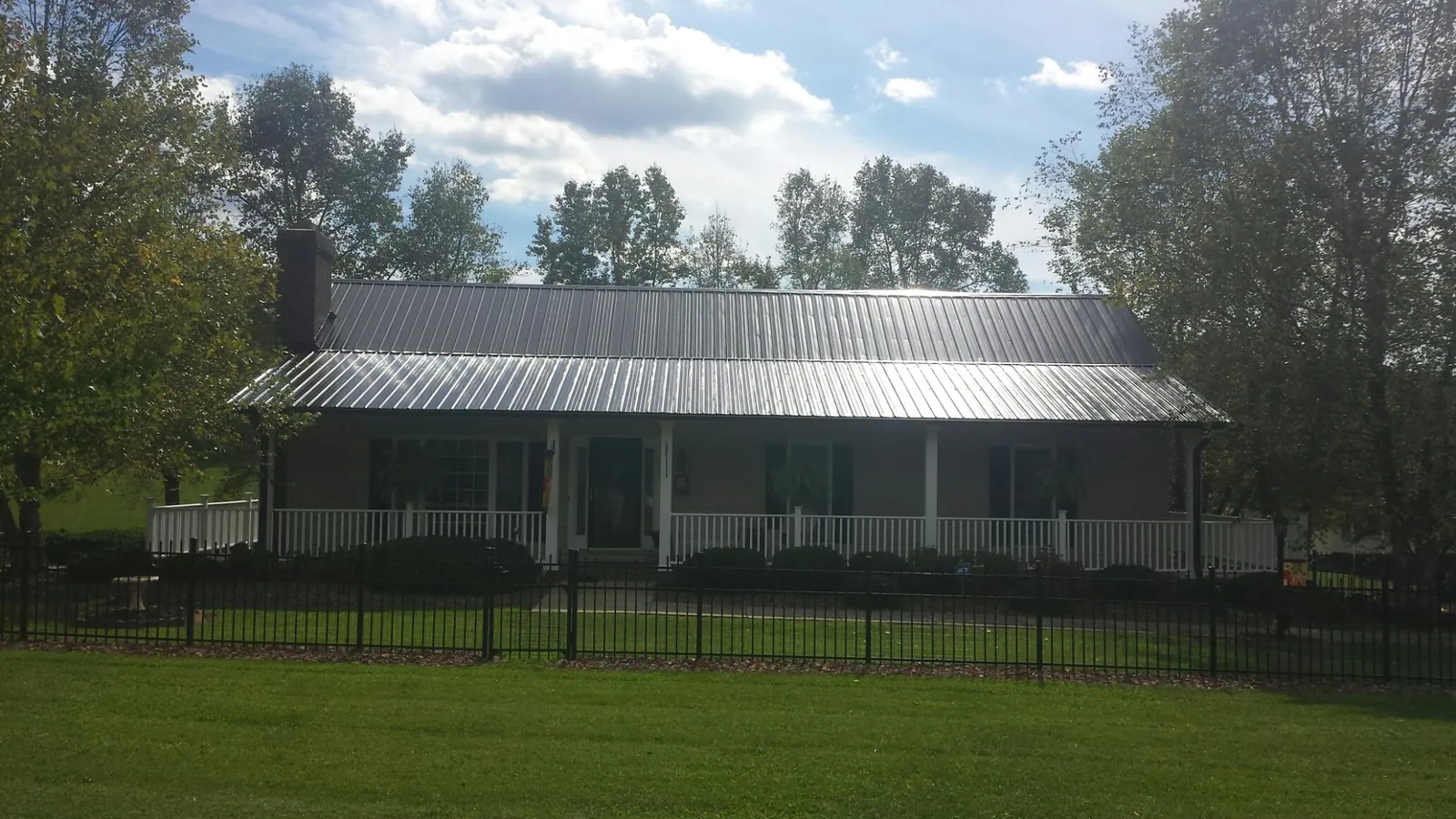 Gray metal roof on a brick ranch with a full width front porch — Gutter Guard Installation work by our crew in Henniker