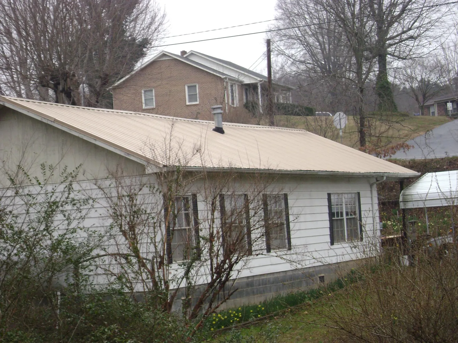 Tan metal roof on a white sided house set into a hillside — Commercial Roofing by Roofing Brothers in Henniker