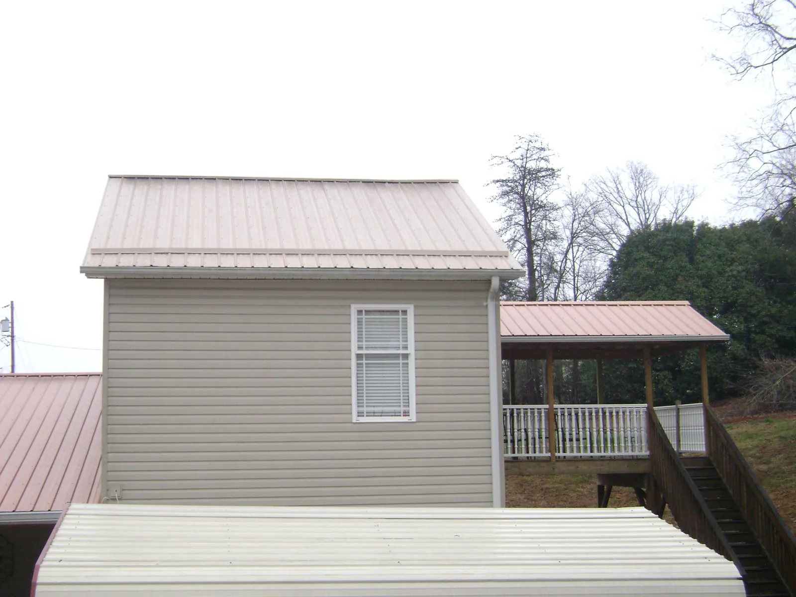 Tan metal roofs on a two story addition and attached porch, from a Roof Replacement job in Henniker